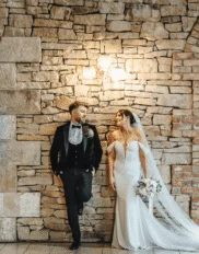 Romantic wedding couple by rustic stone wall at elegant hotel venue.