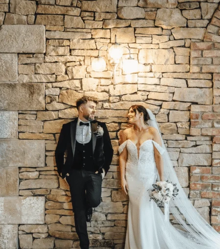 Romantic wedding couple by rustic stone wall at elegant hotel venue.