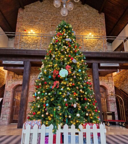 Elegant hotel lobby with festive Christmas tree, twinkling lights, and balcony. Luxurious, welcoming holiday atmosphere.