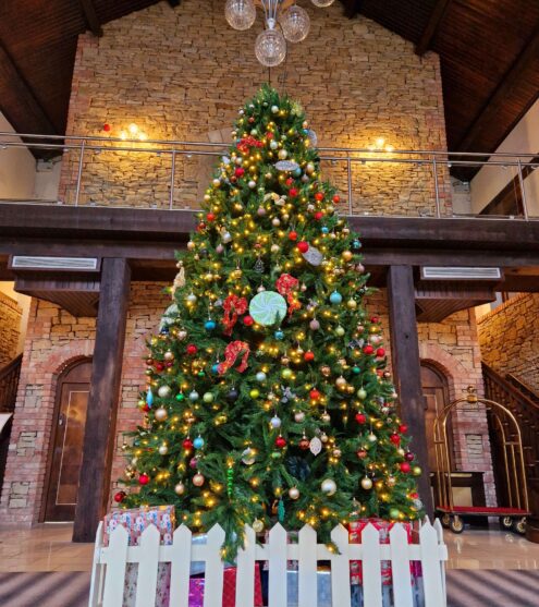 Elegant hotel lobby with festive Christmas tree, twinkling lights, and balcony. Luxurious, welcoming holiday atmosphere.