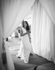 Elegant woman in white dress entering luxurious hotel event space, holding a glass, surrounded by flowing curtains.