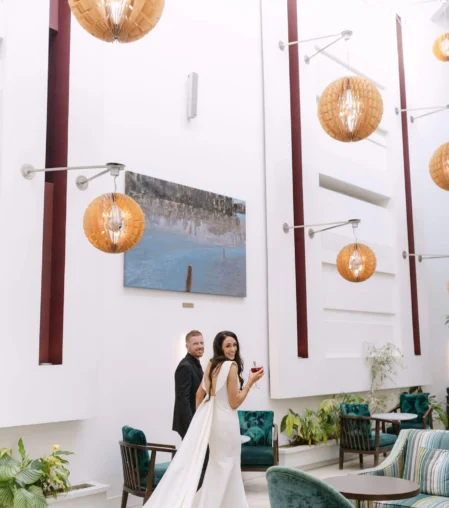 Couple in elegant hotel lounge with high ceilings and modern decor, showcasing ambient lighting and lush greenery.