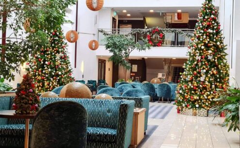 Festive hotel lobby with decorated Christmas trees, cosy seating, and inviting atmosphere for guests.