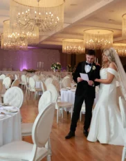 Elegant ballroom with chandeliers, bride and groom reviewing wedding details; luxury wedding venue in elegant setting.
