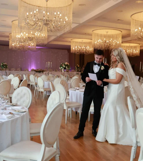 Elegant ballroom with chandeliers, bride and groom reviewing wedding details; luxury wedding venue in elegant setting.